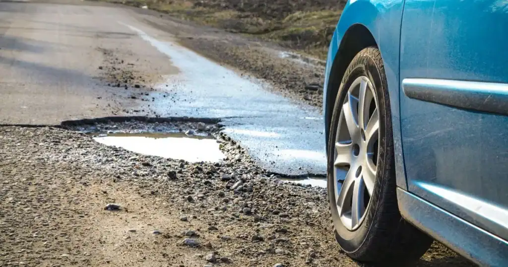 Car near pothole on rough road, potential hazard for drivers.
