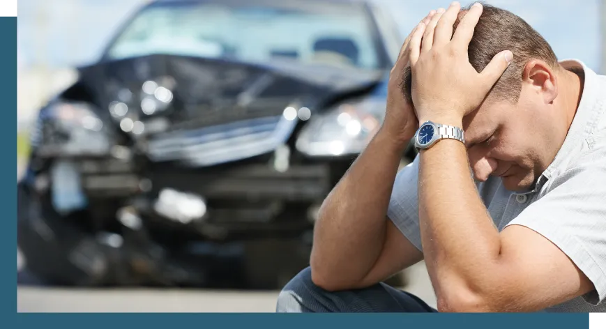 man holding his head in front of a crashed car who is in need of a South Carolina car accident lawyer