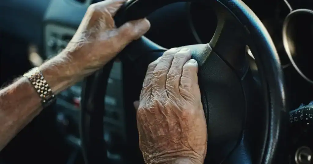 Close-up of elderly person's hands gripping a car steering wheel.
