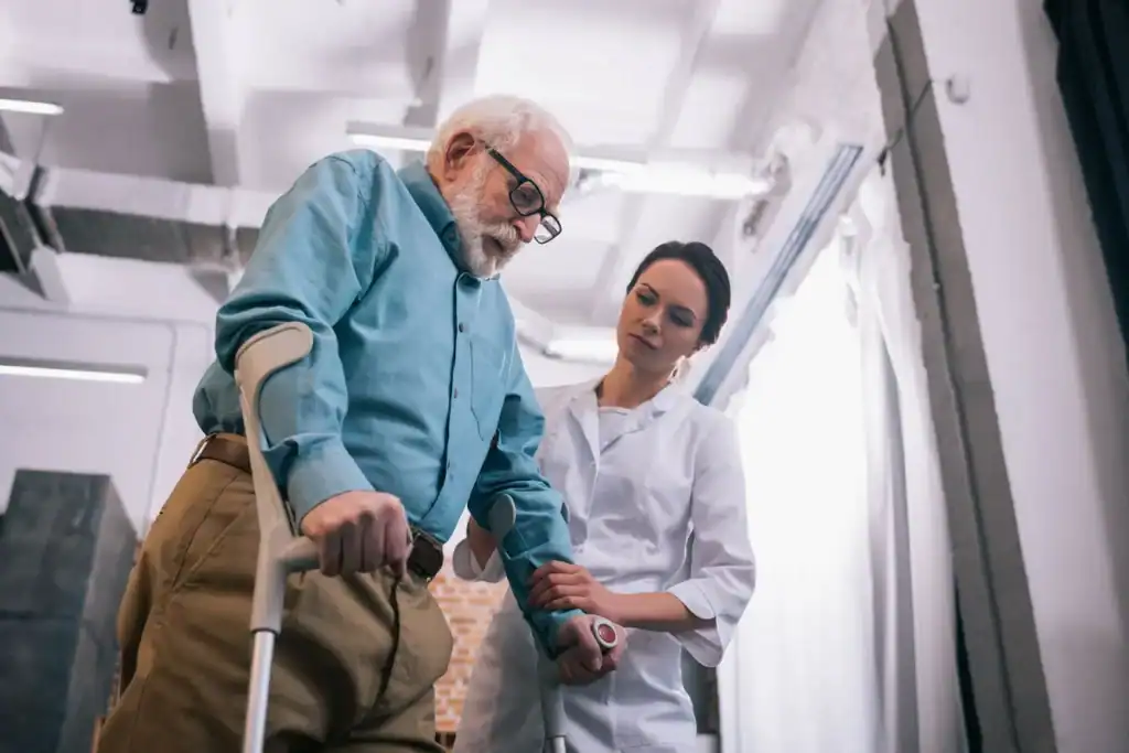 Elderly man with a cane receiving assistance from a healthcare professional in a medical setting.