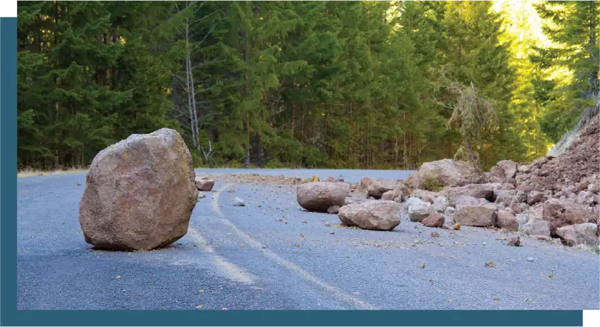 Fallen rocks block a forest road after a storm, creating a hazard for travelers and requiring cleanu.