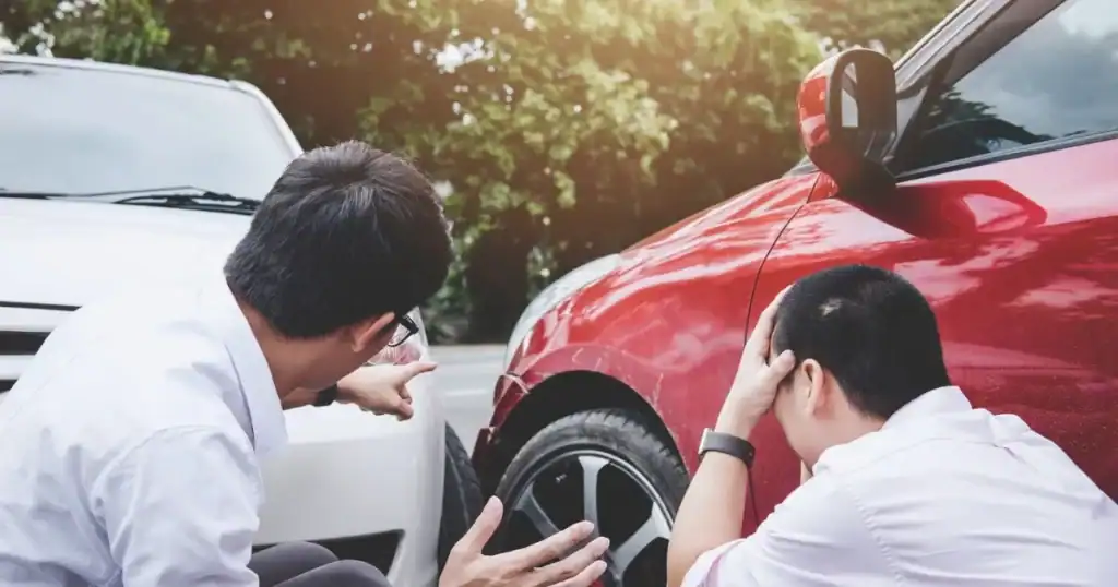 Two men inspecting a car after a minor collision in a parking lot.