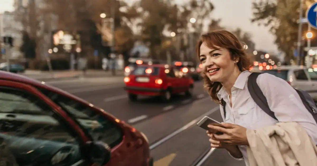 Happy woman waiting for a rideshare in Charleston at dusk.