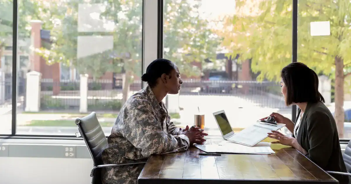 Two women in military uniform and civilian attire discuss asbestos claims at a table.