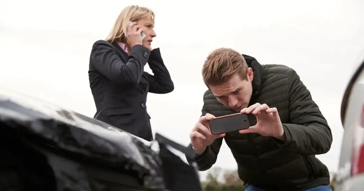 Man and woman inspecting car accident damage and taking photos.
